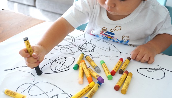 Enfant de 18 mois dessinant avec des feutres lavables sur une feuille blanche sous la supervision bienveillante d'une éducatrice.