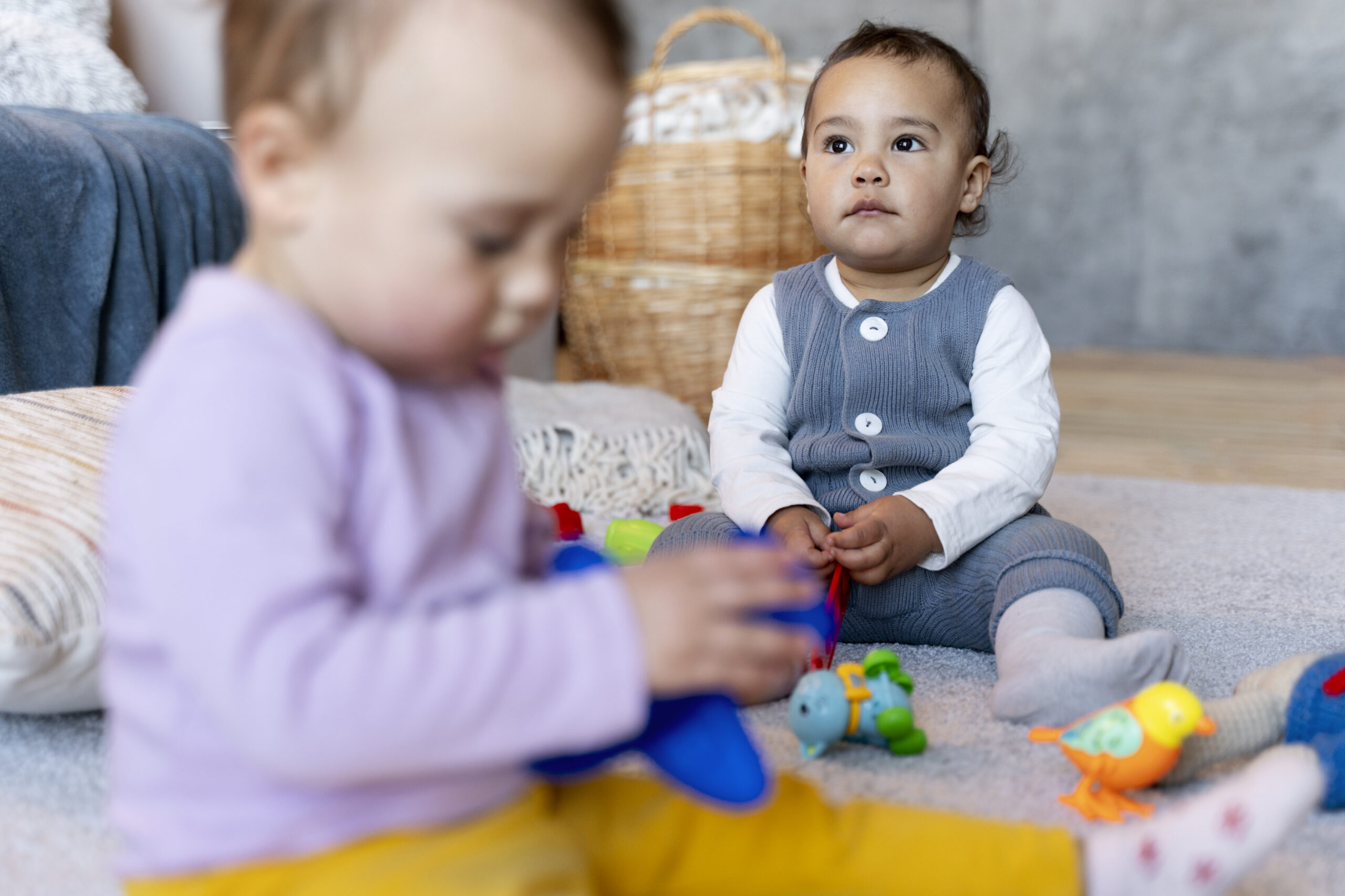 Deux enfants jouant côte à côte et partageant des jouets, sous la supervision d’une éducatrice attentive.