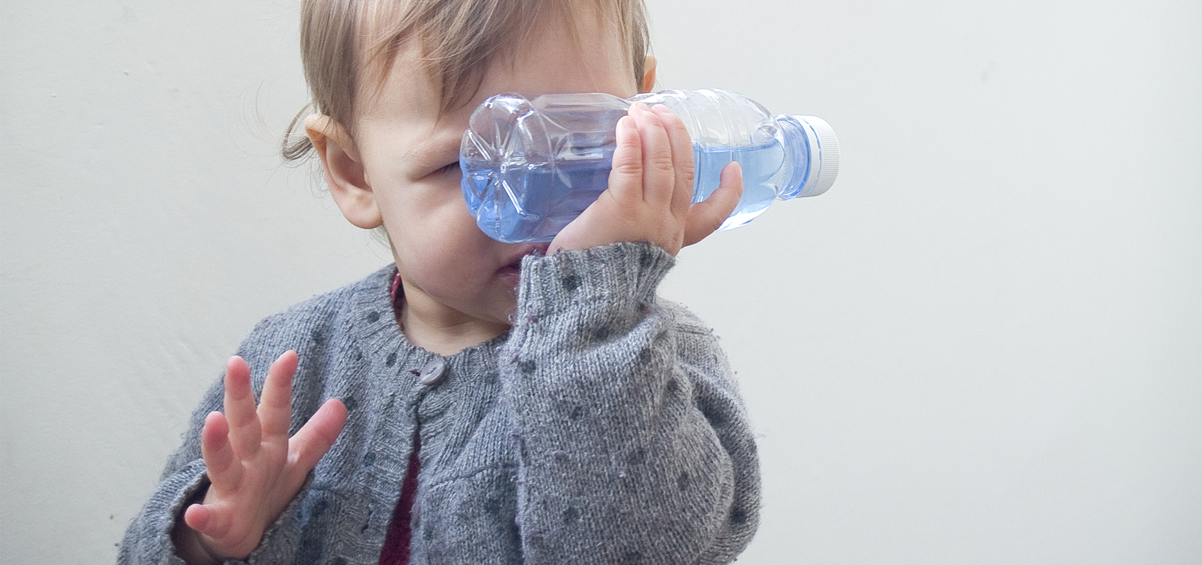 Bébé tenant une bouteille avec du riz coloré, explorant les sons et développant sa motricité fine.